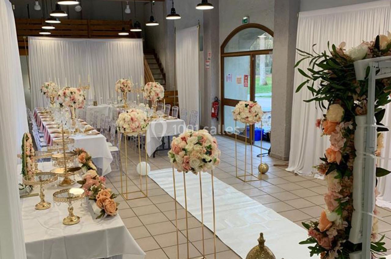 Salle décorée pour un événement avec tables alignées, nappes blanches, compositions florales et allée centrale ornée.