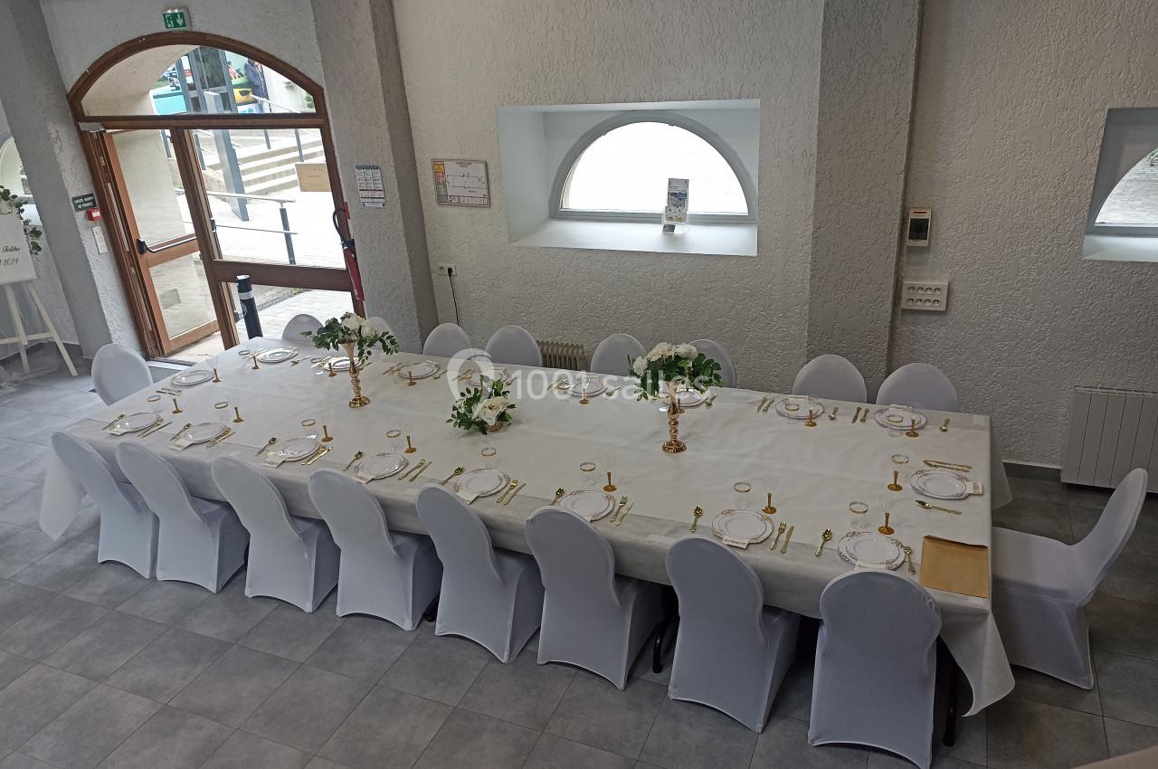 Grande table rectangulaire dressée pour un repas, avec nappes blanches, vaisselle élégante et décorations florales.