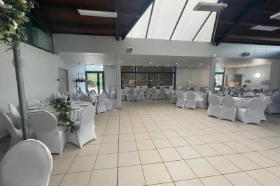 Salle décorée pour un événement avec tables alignées, nappes blanches, compositions florales et allée centrale ornée.