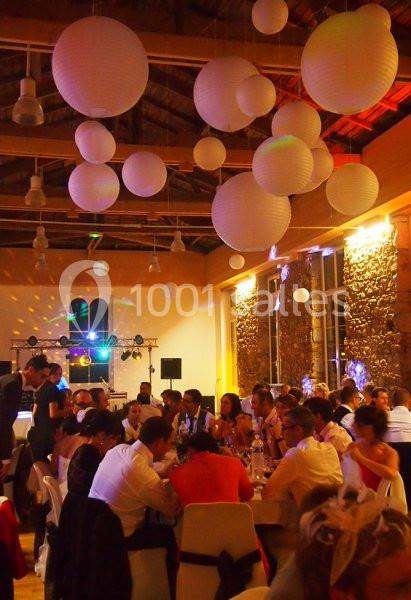 Salle de réception décorée de lanternes suspendues, avec des invités assis à des tables lors d'un événement festif.