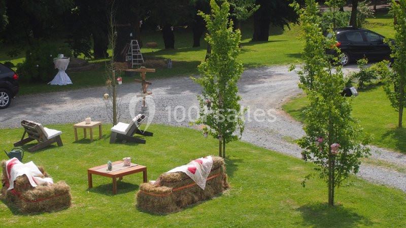 Espace extérieur aménagé avec des bottes de foin, des tables et des chaises, entouré de verdure et d'arbres.