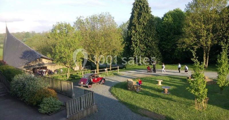 Vue d'un espace extérieur avec pelouse, arbres, une voiture ancienne rouge et des personnes se promenant.