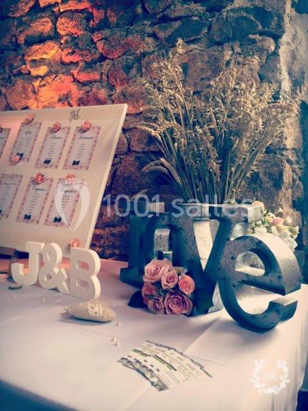 Décoration de mariage avec des initiales, des fleurs, un vase en métal ’love’ et un tableau de plan de table.