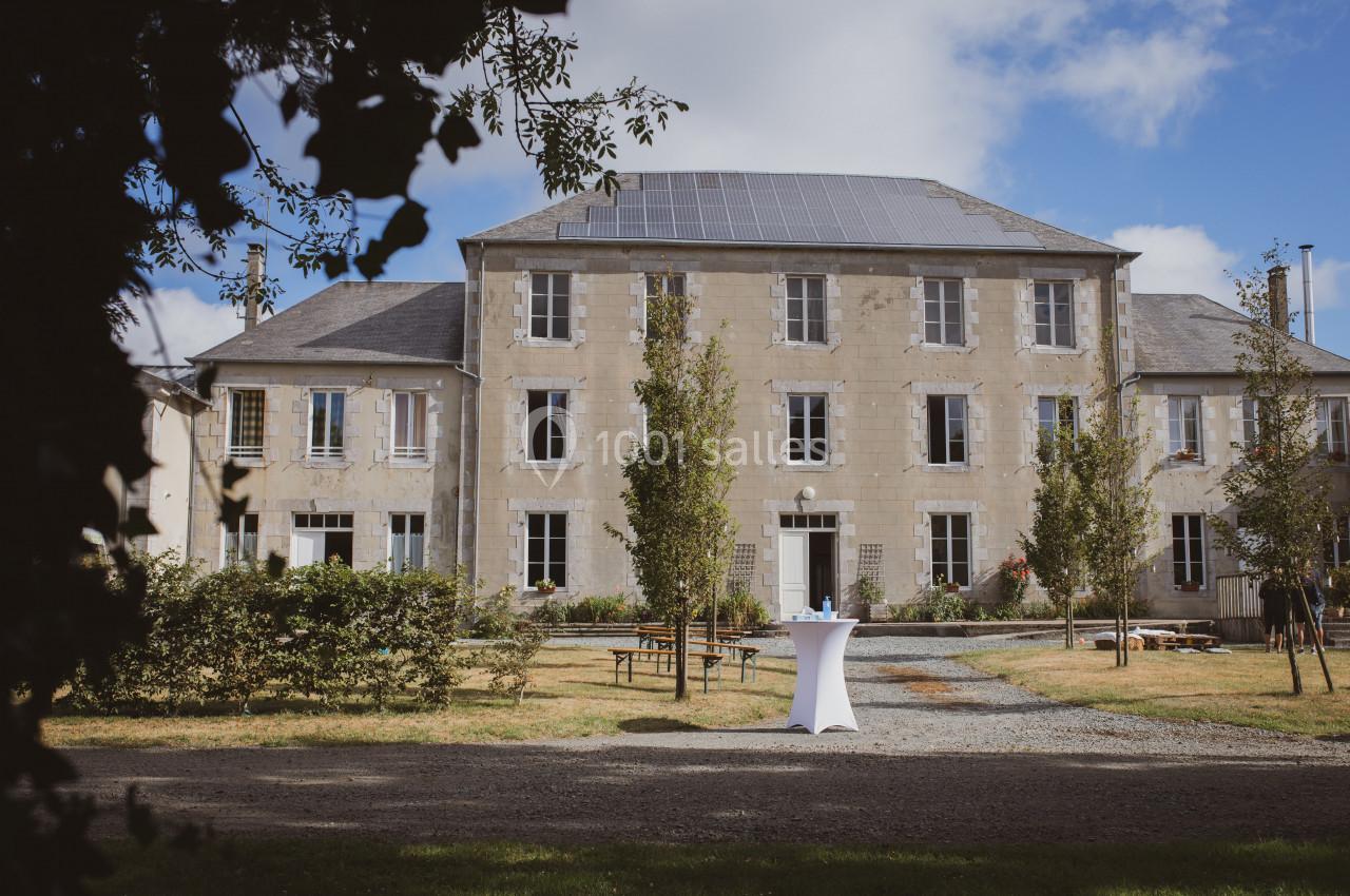 Façade d'un grand bâtiment en pierre entouré d'arbres, avec une table haute blanche au premier plan.