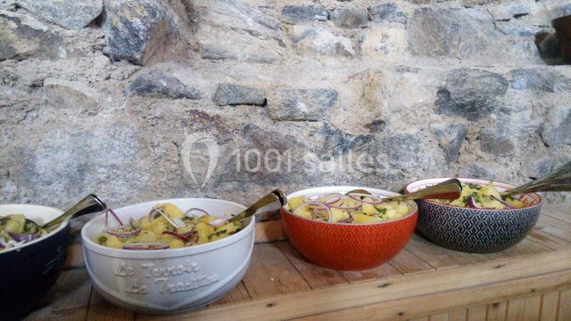 Quatre saladiers contenant de la salade de pommes de terre avec oignons rouges, posés sur une table en bois devant un mur en…