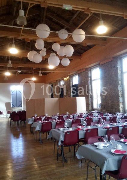 Salle de réception avec tables dressées, chaises rouges, nappes grises et suspensions lumineuses rondes au plafond.