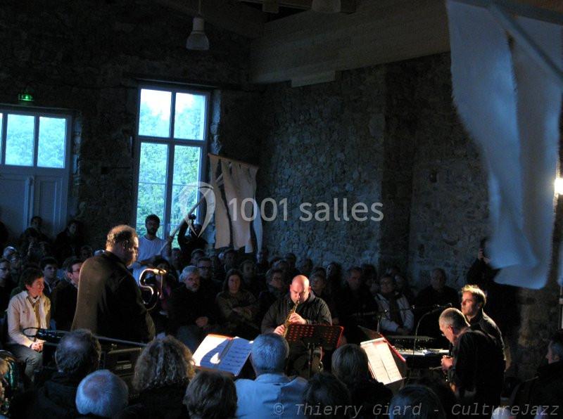 Un groupe de musiciens joue devant un public assis dans une salle en pierre avec des fenêtres éclairées.