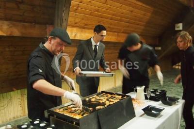 Vue d'un espace extérieur avec pelouse, arbres, une voiture ancienne rouge et des personnes se promenant.