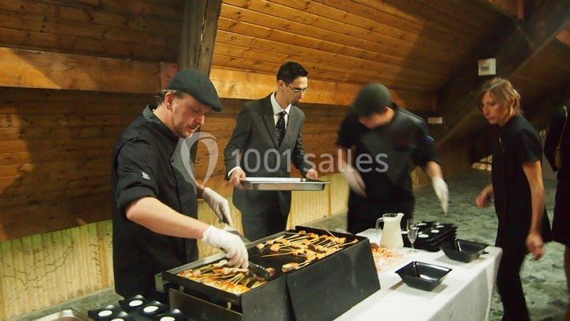 Des cuisiniers préparent et servent des brochettes sur un gril lors d'un événement dans un espace en bois.