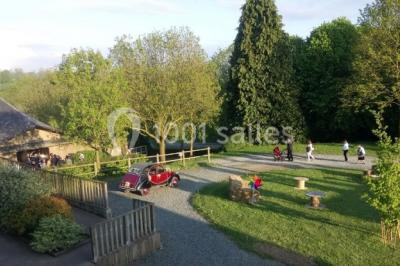 Vue d'un espace extérieur avec pelouse, arbres, une voiture ancienne rouge et des personnes se promenant.