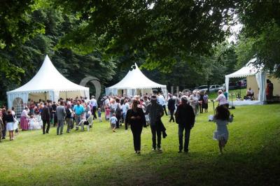 Vue d'un espace extérieur avec pelouse, arbres, une voiture ancienne rouge et des personnes se promenant.