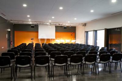 Parking vide devant un bâtiment moderne gris avec l'enseigne ’Le Dastala’ et des arbres en arrière-plan.