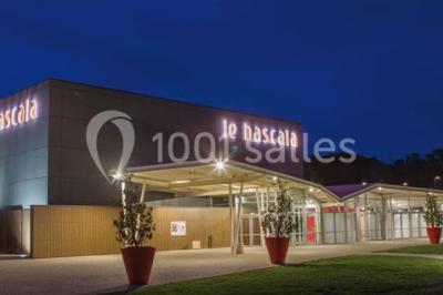 Parking vide devant un bâtiment moderne gris avec l'enseigne ’Le Dastala’ et des arbres en arrière-plan.