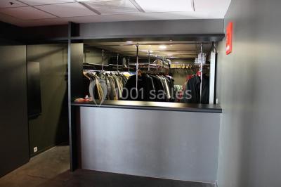 Parking vide devant un bâtiment moderne gris avec l'enseigne ’Le Dastala’ et des arbres en arrière-plan.