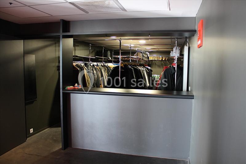 Vestiaire avec comptoir noir, portant des vêtements suspendus sur des cintres dans un espace sombre.