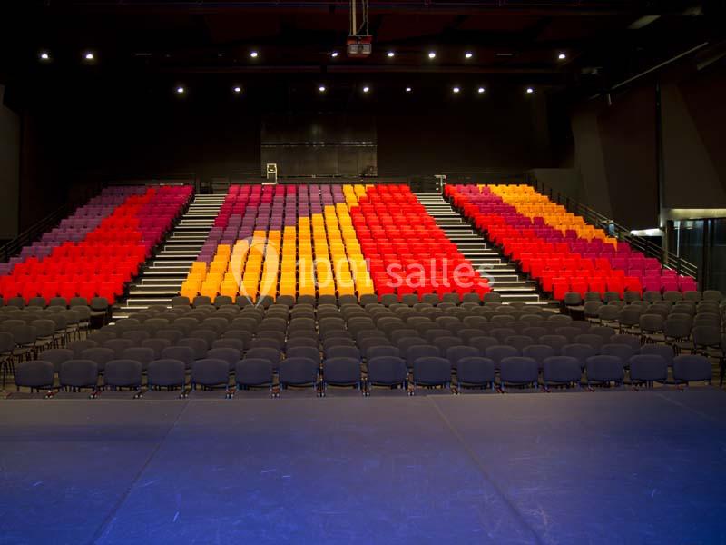 Gradins colorés avec des sièges rouges, orange et violets, devant une scène vide dans une salle de spectacle moderne.