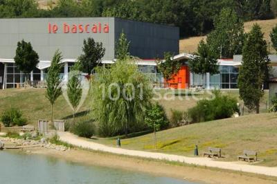 Parking vide devant un bâtiment moderne gris avec l'enseigne ’Le Dastala’ et des arbres en arrière-plan.