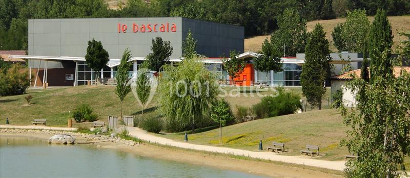 Bâtiment moderne entouré d'arbres, situé près d'un chemin et d'un plan d'eau, avec l'inscription ’Le Bascala’.