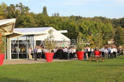 Parking vide devant un bâtiment moderne gris avec l'enseigne ’Le Dastala’ et des arbres en arrière-plan.