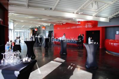 Parking vide devant un bâtiment moderne gris avec l'enseigne ’Le Dastala’ et des arbres en arrière-plan.