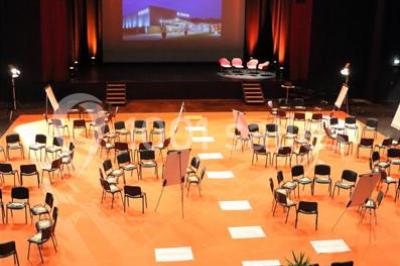 Parking vide devant un bâtiment moderne gris avec l'enseigne ’Le Dastala’ et des arbres en arrière-plan.
