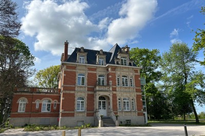 Cérémonie en plein air dans un parc, avec des invités assis face à une mariée et un officiant, devant un manoir.