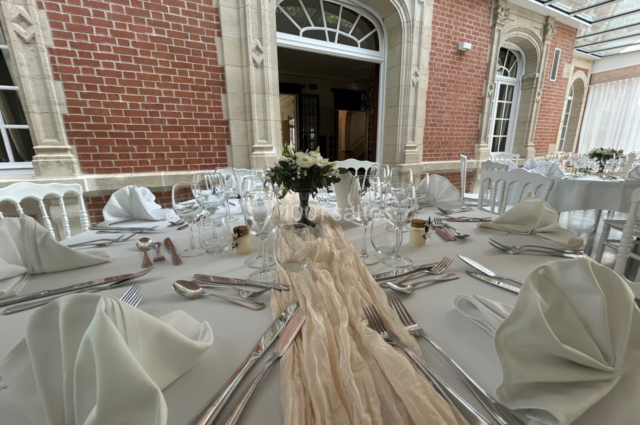 Table élégamment dressée avec nappes blanches, serviettes pliées, couverts en argent et centre de table floral dans une…