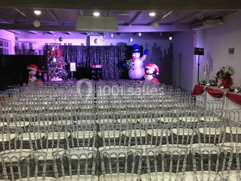 Salle décorée pour Noël avec des rangées de chaises transparentes, un sapin illuminé et des bonshommes de neige en arrière…
