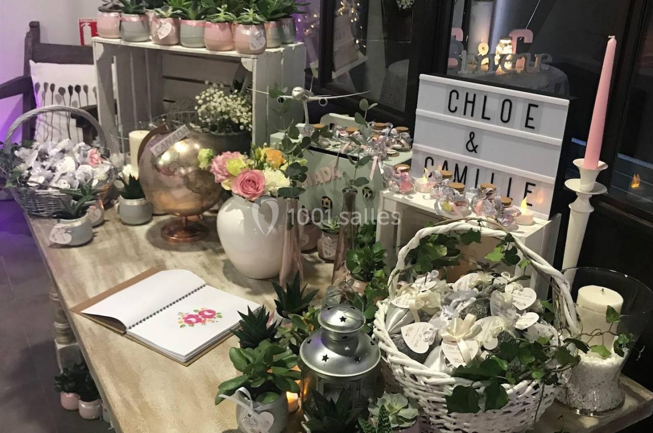 Table décorée avec des plantes, bougies, fleurs, et une boîte lumineuse affichant ’Chloé & Camille’.