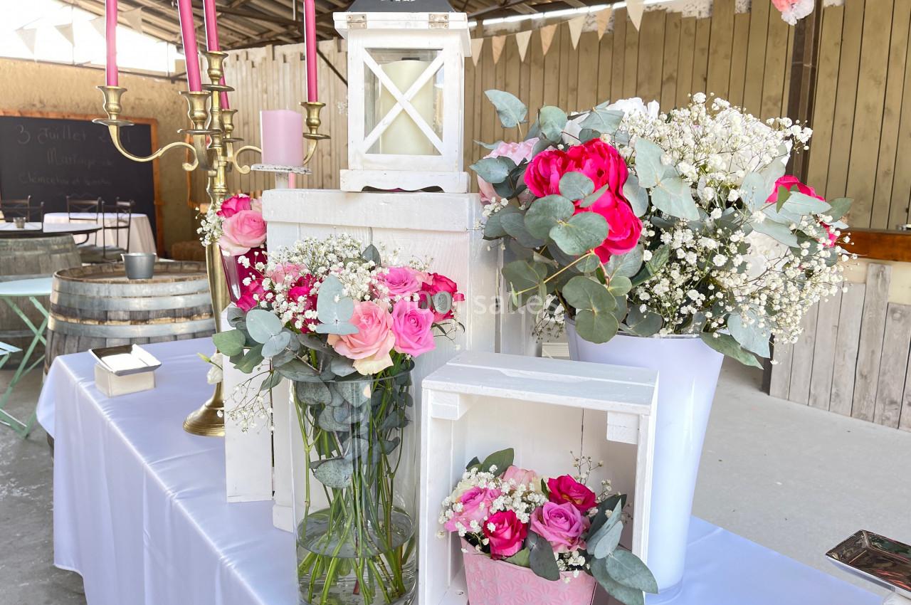 Décoration florale avec roses roses et rouges, gypsophiles et feuillage, disposée sur une table dans un cadre rustique.