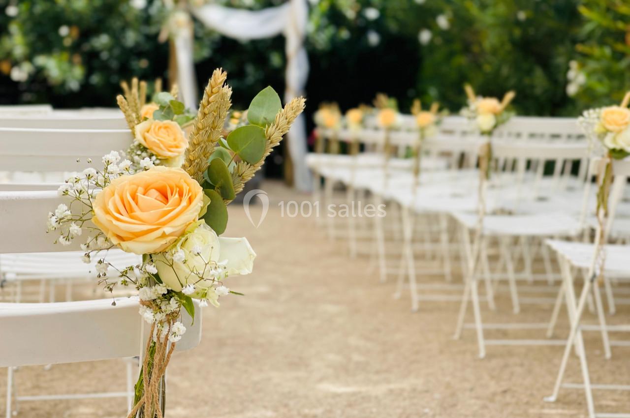 Chaises blanches alignées pour une cérémonie en extérieur, décorées de roses jaunes et de feuillages.