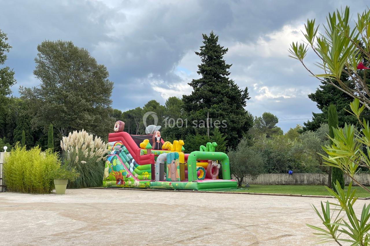 Structure gonflable colorée avec toboggan dans un espace extérieur arboré sous un ciel nuageux.