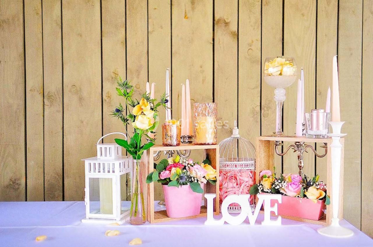 Décoration de table avec fleurs, bougies, lanternes et lettres formant le mot ’LOVE’ devant un fond en bois clair.