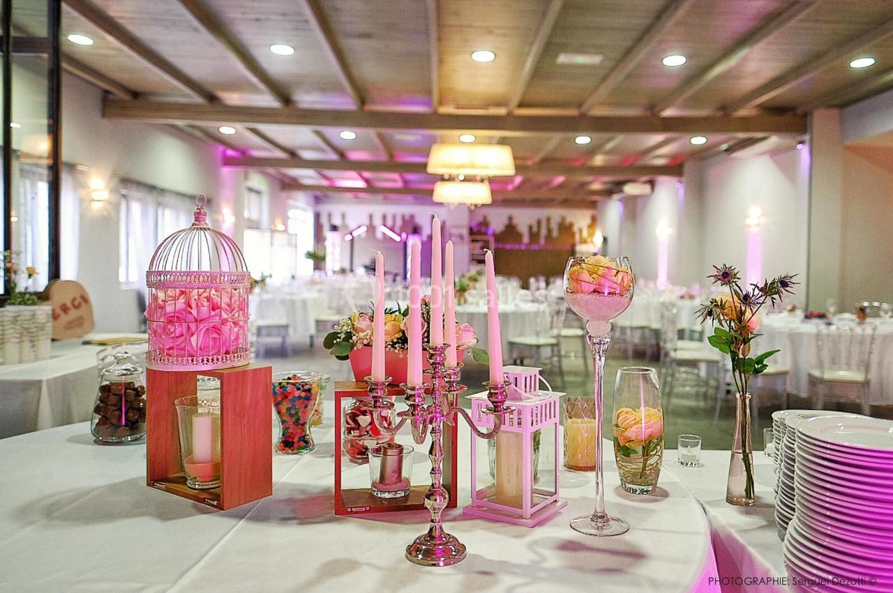 Décoration de table avec bougies, bonbonnières et fleurs dans une salle de réception lumineuse et élégante.