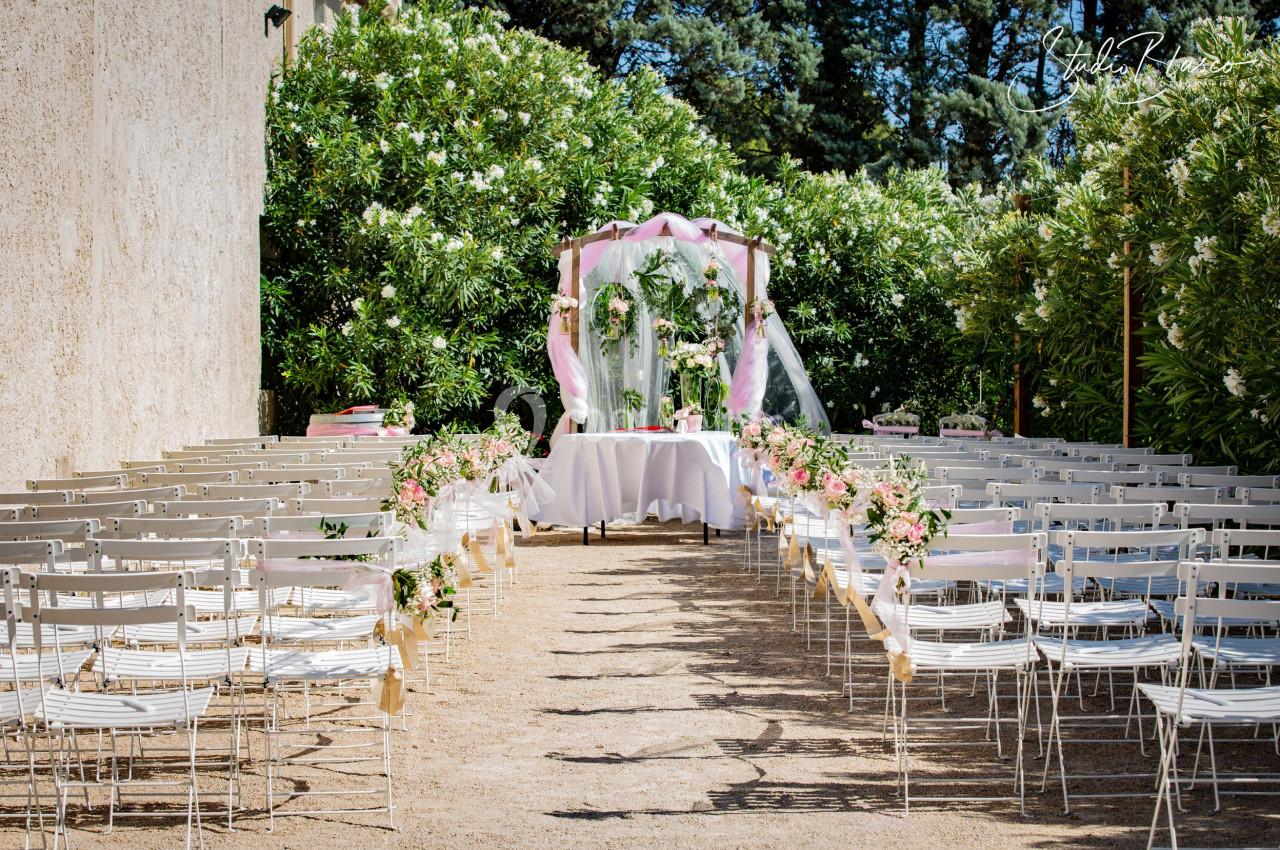 Allée centrale bordée de chaises blanches menant à une arche décorée de fleurs et de voilages pour une cérémonie en plein…