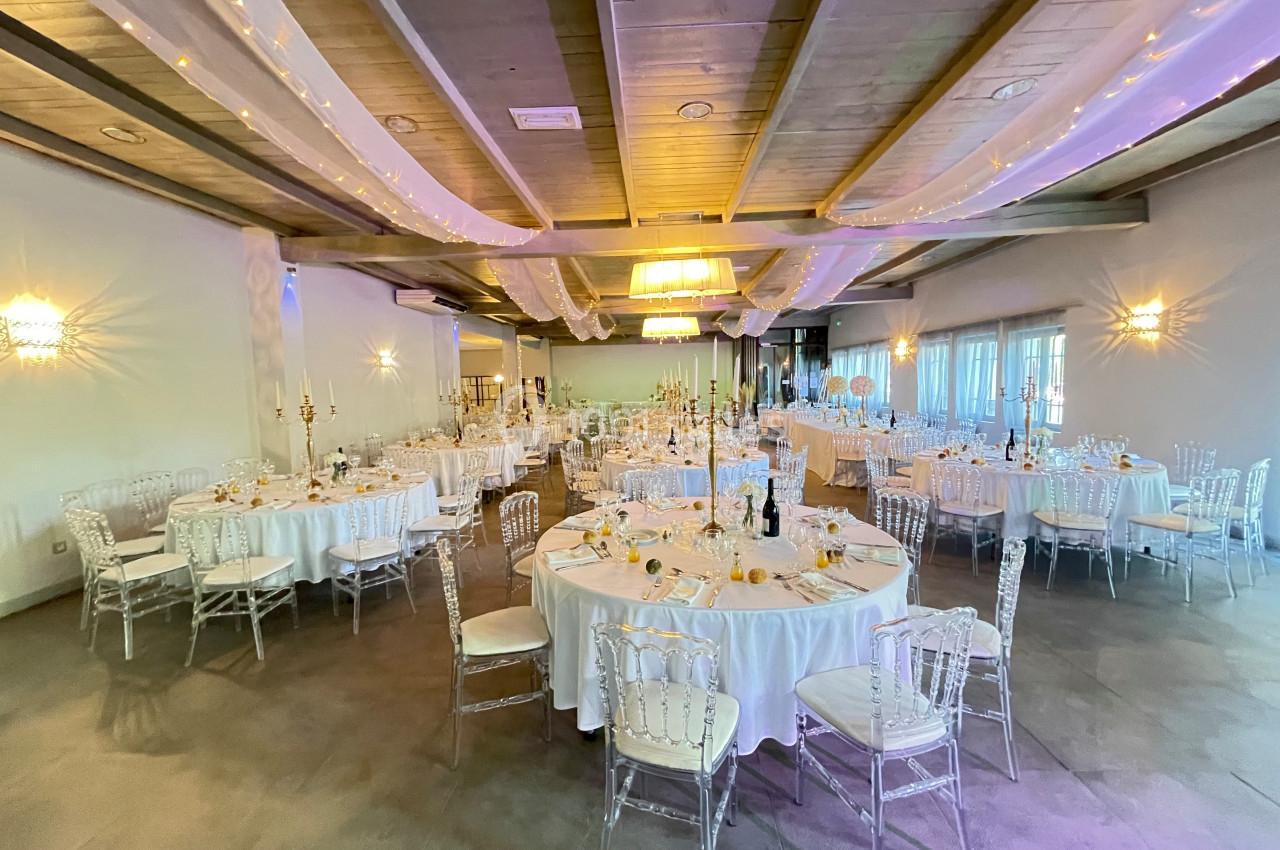 Salle de réception décorée avec des tables rondes dressées, chaises transparentes et éclairage tamisé.