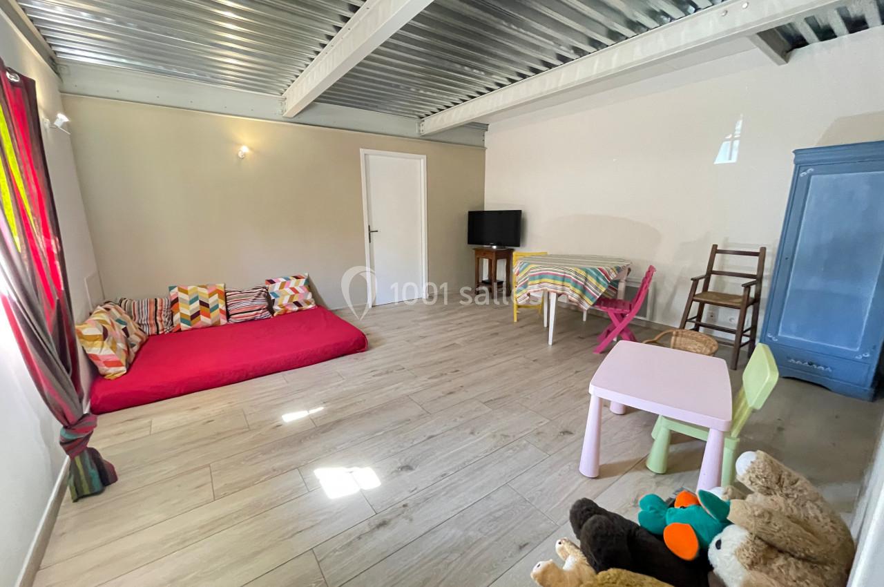 Salle lumineuse avec sol en bois, matelas au sol, table avec chaises, armoire bleue et jouets pour enfants.