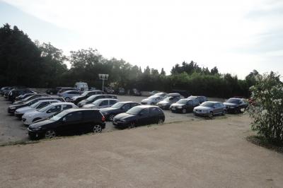 Un parking extérieur rempli de voitures, entouré de végétation et éclairé par une lumière naturelle.