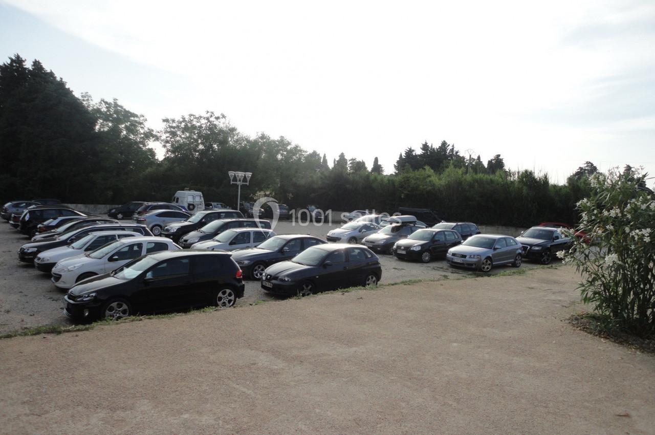 Un parking extérieur rempli de voitures, entouré de végétation et éclairé par une lumière naturelle.