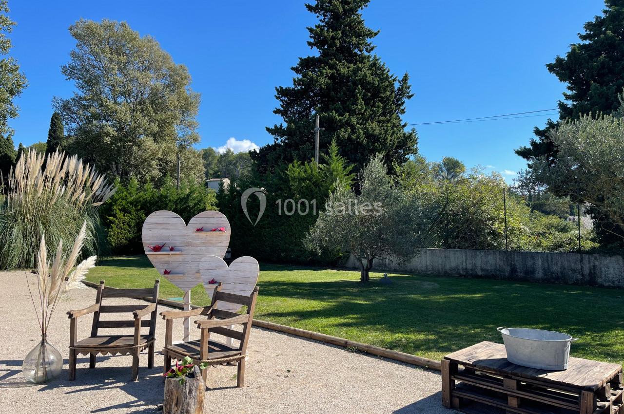 Espace extérieur avec chaises en bois, décorations en forme de cœur, pelouse, arbres et ciel dégagé en arrière-plan.