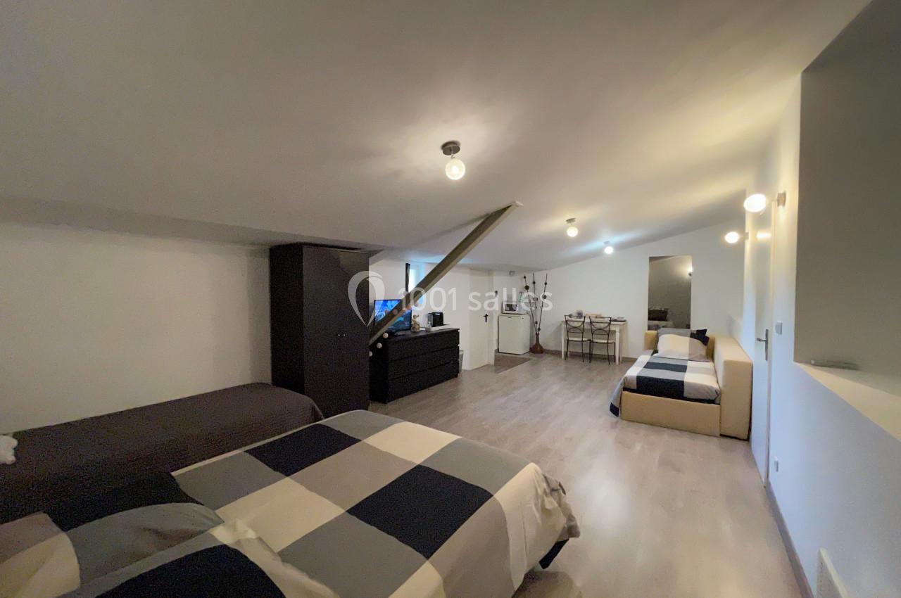 Chambre mansardée avec deux lits, un canapé, une table à manger et un éclairage suspendu, décor moderne et épuré.