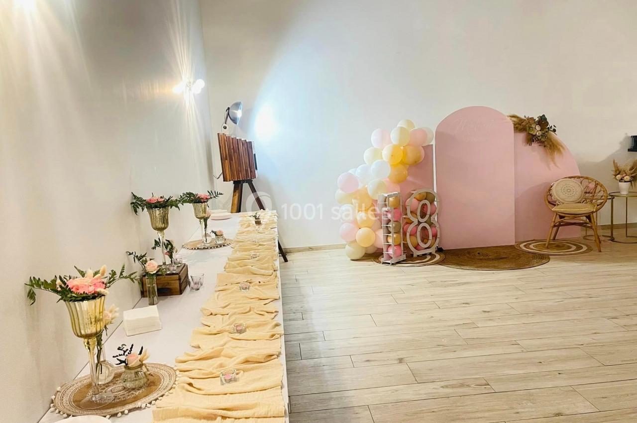 Table décorée avec des nappes et des fleurs, ballons pastel et panneau rose en arrière-plan dans une salle lumineuse.