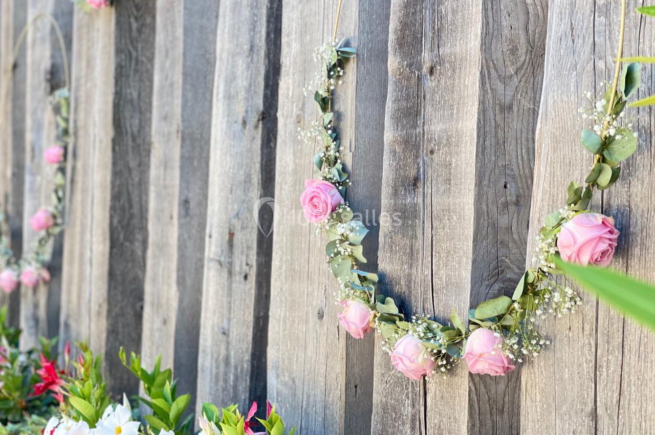 Guirlandes de fleurs roses suspendues sur une clôture en bois, avec des plantes colorées en bas.