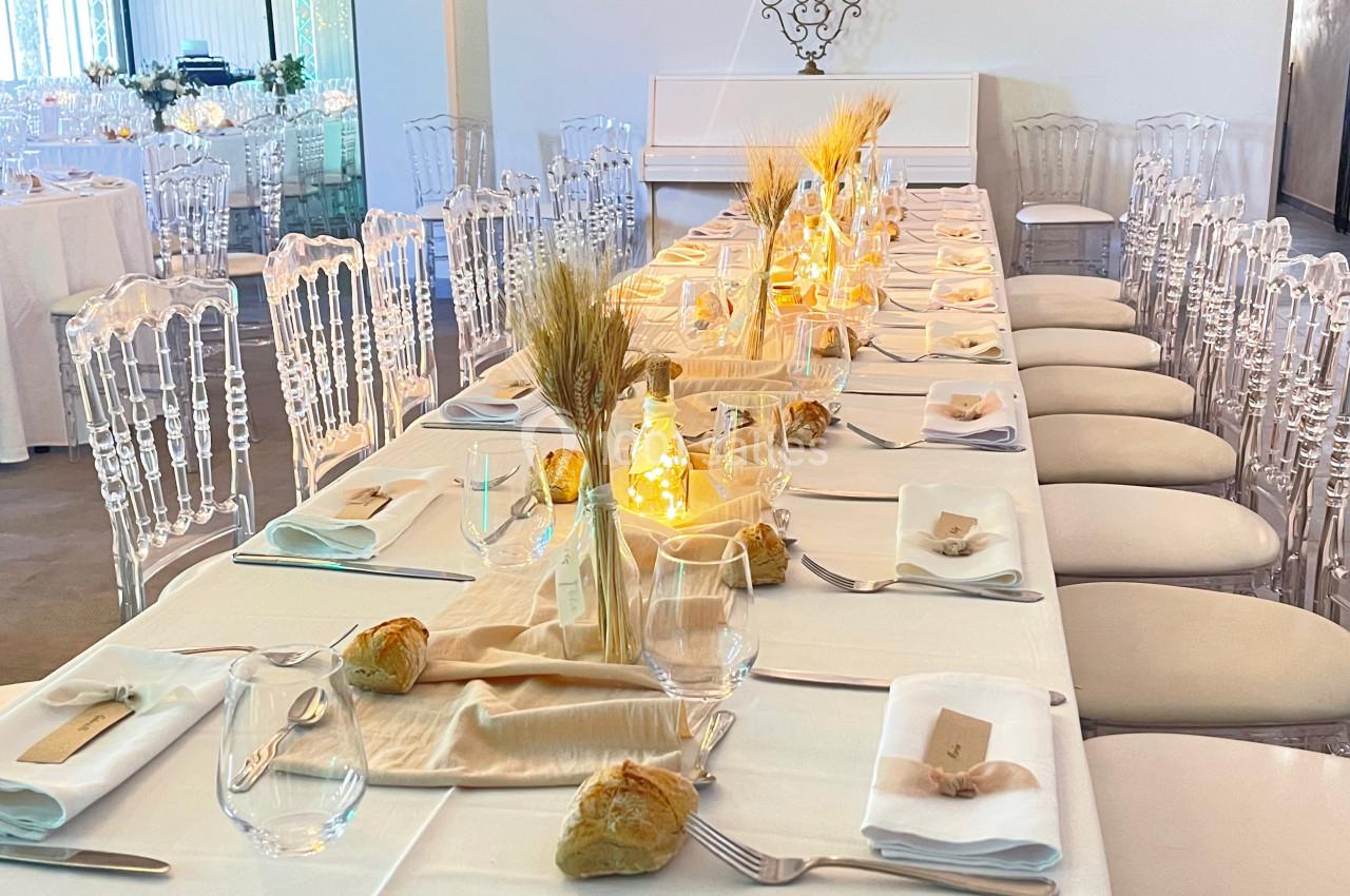 Table de réception élégamment dressée avec nappes blanches, décorations lumineuses et épis de blé en centre de table.