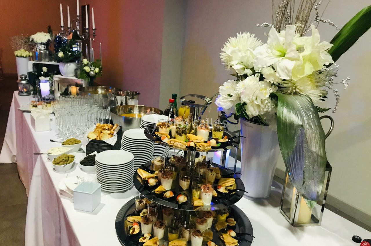 Buffet élégant avec verrines, amuse-bouches, fleurs blanches et chandeliers dans une salle de réception.