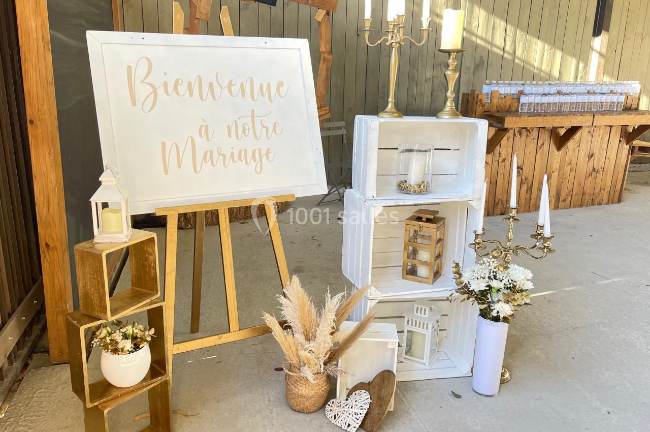 Décoration de mariage avec panneau de bienvenue, bougies, fleurs séchées et caisses en bois dans un espace extérieur.