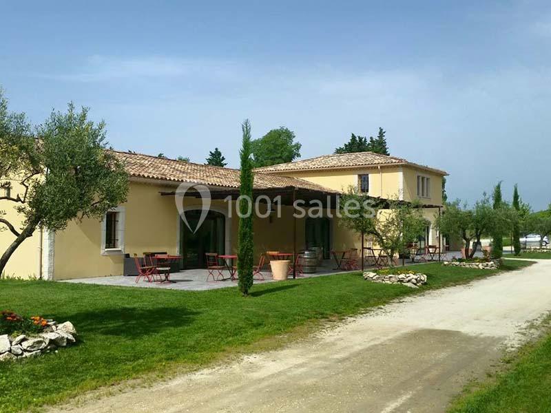 Bâtisse provençale entourée d'oliviers, avec terrasse aménagée et chemin de gravier bordé de pelouse.