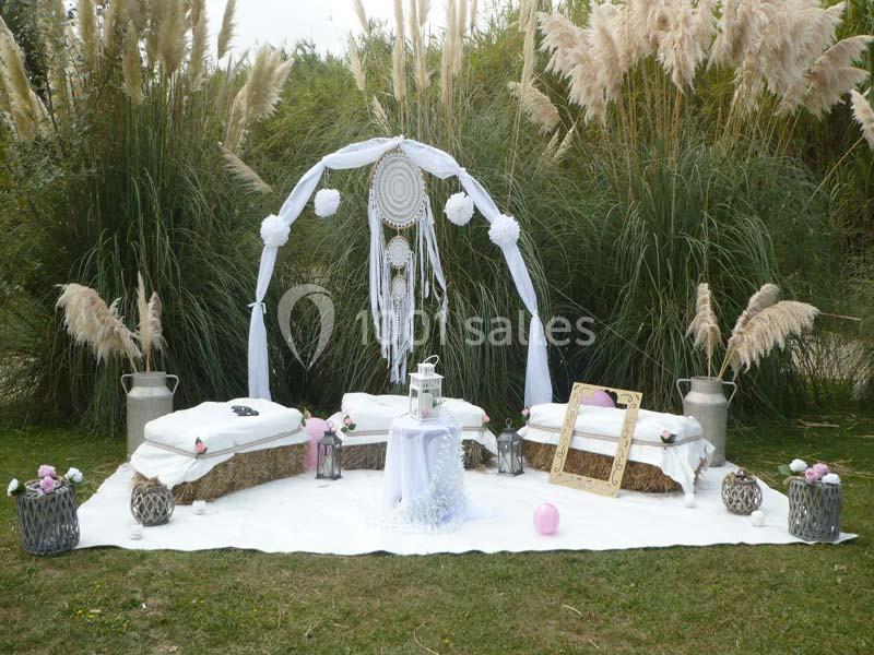 Décoration bohème en extérieur avec arche ornée de plumes, coussins, lanternes et cadre doré sur une pelouse.