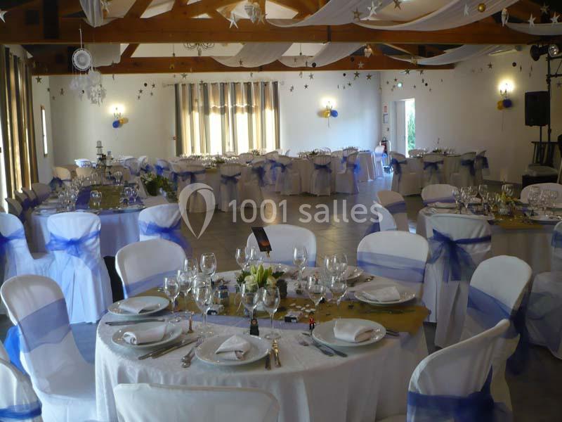 Salle de réception décorée avec des tables rondes dressées, nappes blanches et rubans bleus sur les chaises.