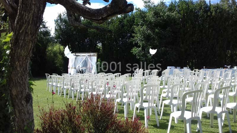 Chaises blanches disposées en rangées sur une pelouse, face à une arche décorée pour une cérémonie en extérieur.